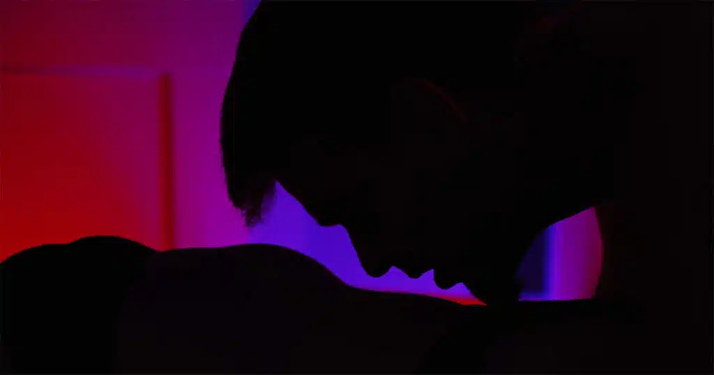 Silhouette of a man kissing a stomach with neon lights in the background